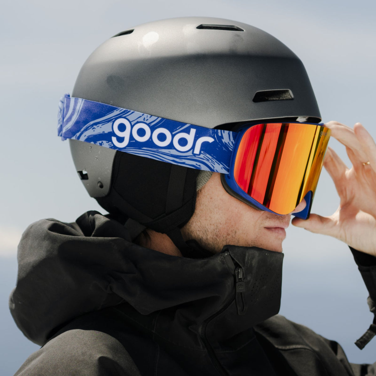 Side view of a person wearing Amber Mountains Majesty | goodr ski goggles with vibrant amber-orange mirrored lenses and a grey helmet.
