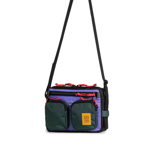 Topo Designs Block Bag in purple, black, and green with a black shoulder strap and red zipper pulls, front view.