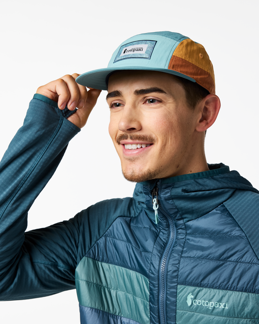 Man wearing a Zen Garden Tech 5-Panel Hat by Cotopaxi in mint green and brown, with a matching jacket.