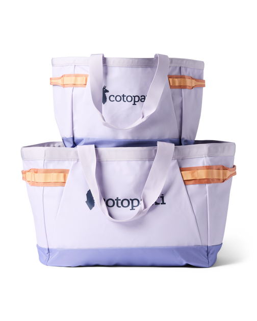 Two lavender Cotopaxi Allpa 60L Gear Hauler Tote bags, stacked, with orange accents and a purple base.