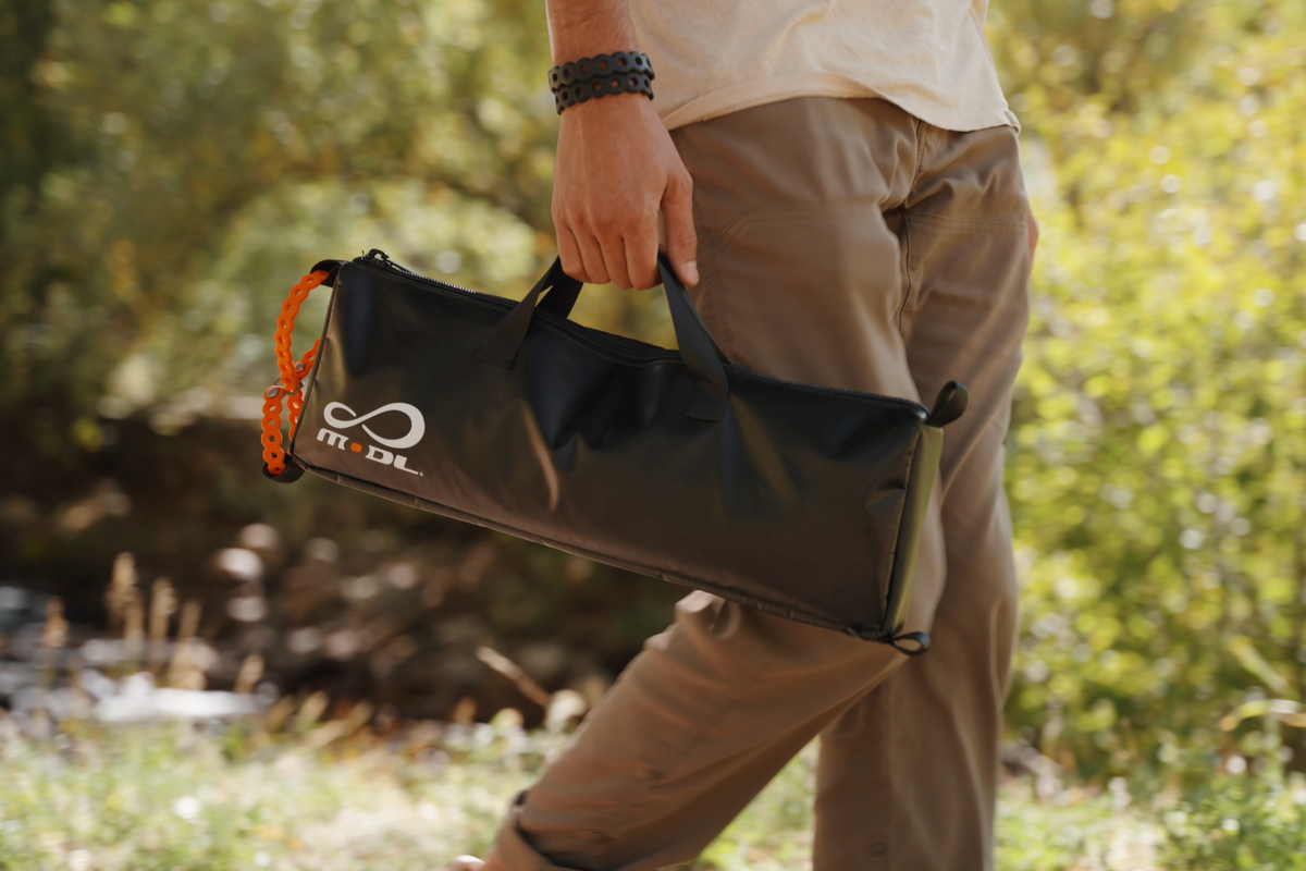 Person walking outdoors holding the black MODL Infinity ToolKit™ with an orange accessory, surrounded by green foliage.