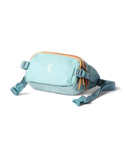 Cotopaxi Allpa X 1.5L Hip Pack in a serene light blue color, featuring orange zipper pulls and an adjustable waist strap.
