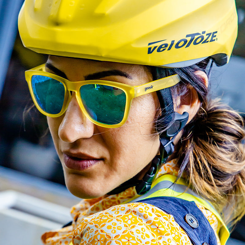 Close-up of a person wearing 'Swedish Meatball Hangover' goodr sunglasses, a yellow helmet, and a patterned shirt.