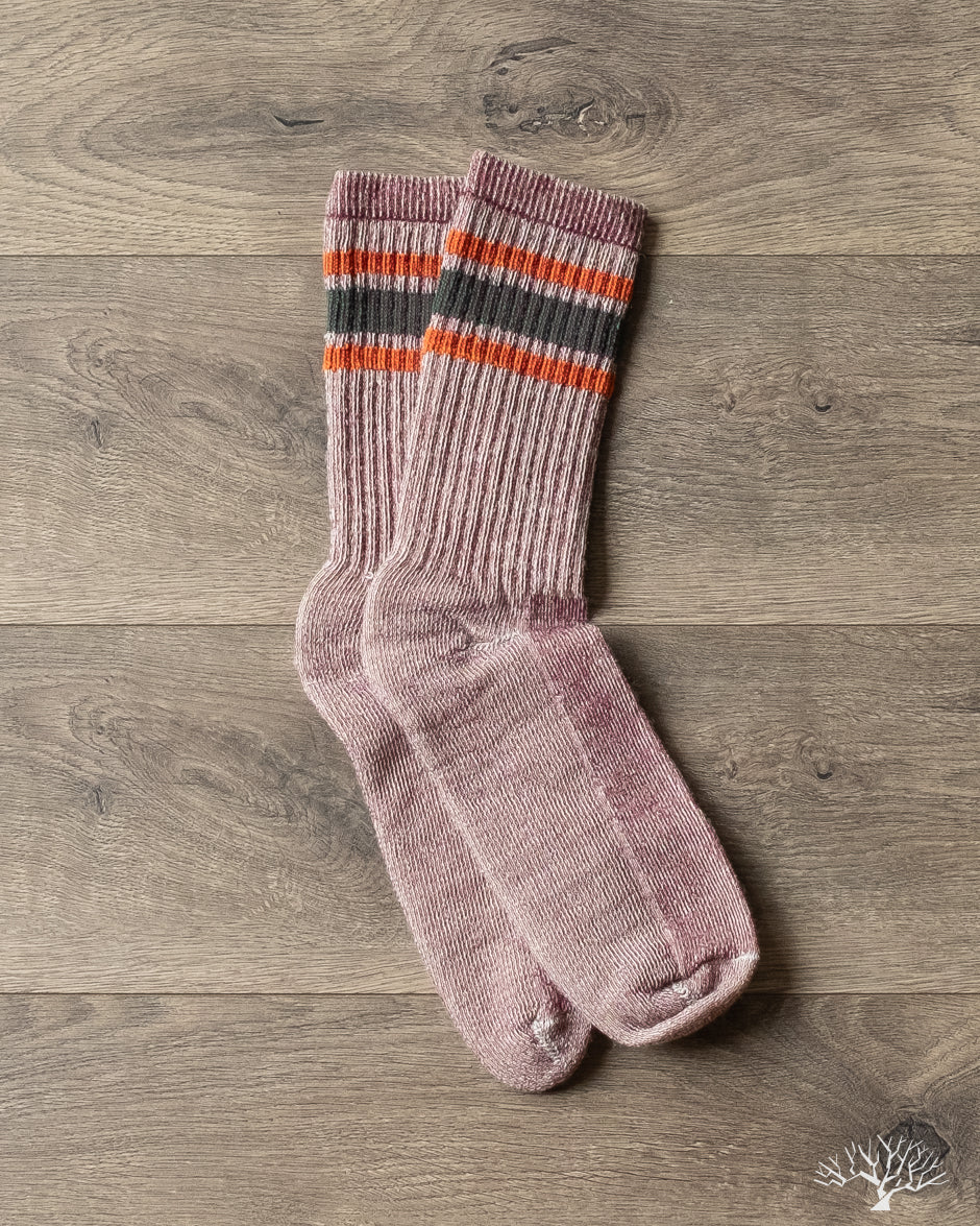 A pair of pink Merino Activity Crew socks by American Trench with orange and dark grey stripes, lying on a wooden surface.
