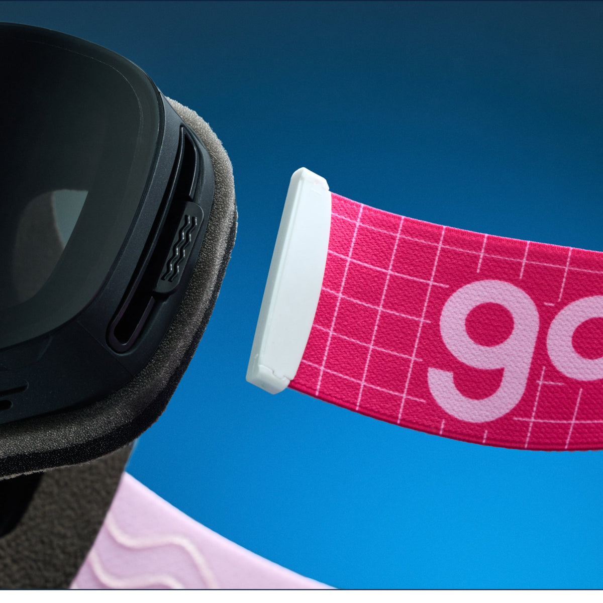 Close-up of goodr Slush Bunny Pinkout ski goggles, showing the pink strap with grid pattern and goodr logo against a blue background.