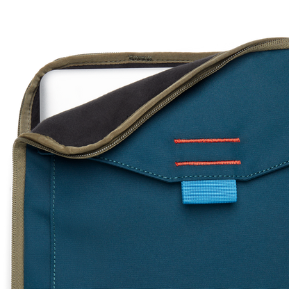 Close-up of a blue Cotopaxi Cada Dia 16" Laptop Sleeve with a laptop partially inserted, showing khaki zipper and blue tag.