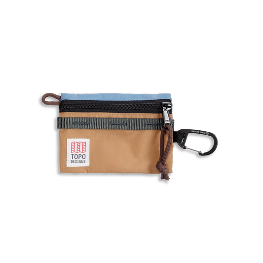 Topo Designs Mountain Accessory Bag with light blue, tan, and black panels, a zipper closure, logo, and carabiner clip.
