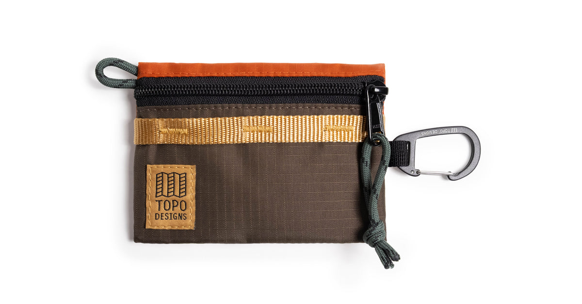 Topo Designs Mountain Accessory Bag in brown, orange, and gold with a black zipper and carabiner, on white.