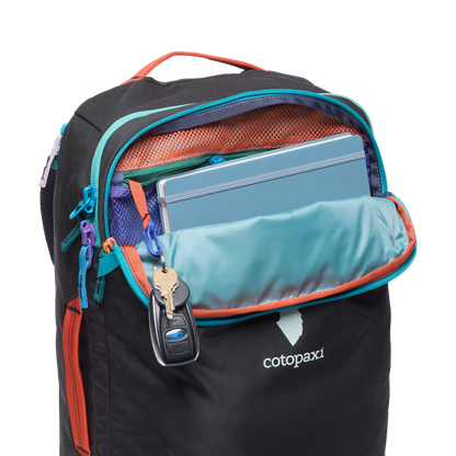Cotopaxi Allpa 28L Travel Pack in black with an open top compartment showing a blue notebook and keys hanging inside.