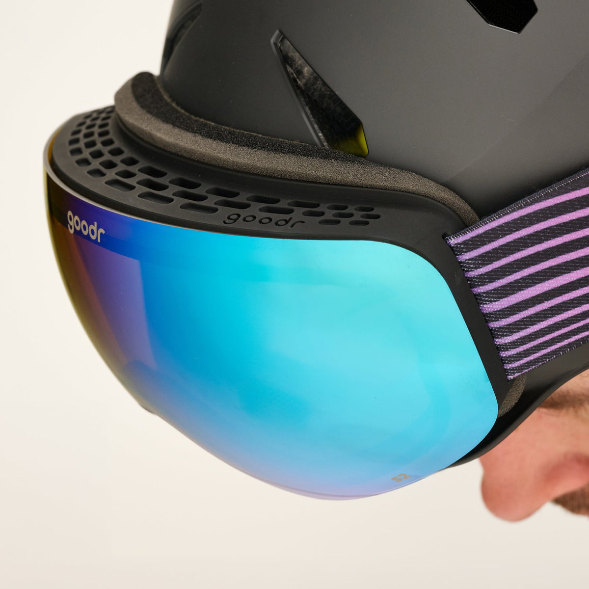 Close-up of "Alpine State of Mind | goodr" ski goggles with a blue-purple mirrored lens attached to a black helmet.