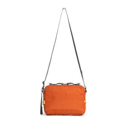 Topo Designs Block Bag in orange with a grey adjustable strap, hanging. Front view of a versatile utility pouch.