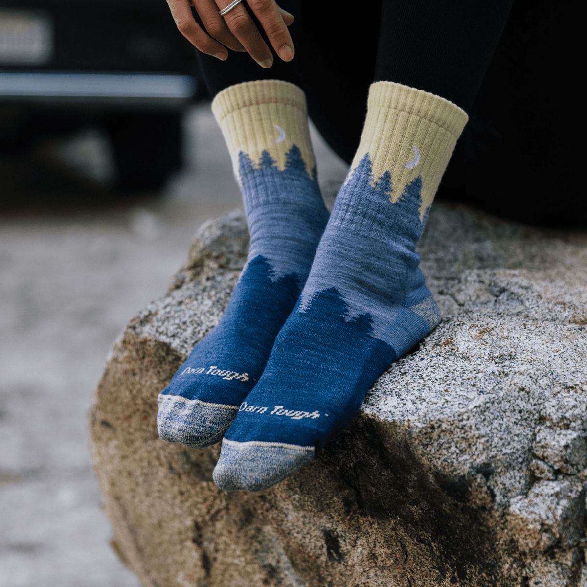 Close-up of Women's Treeline Micro Crew Darn Tough socks with blue treeline and moon design worn by a person on a rock.