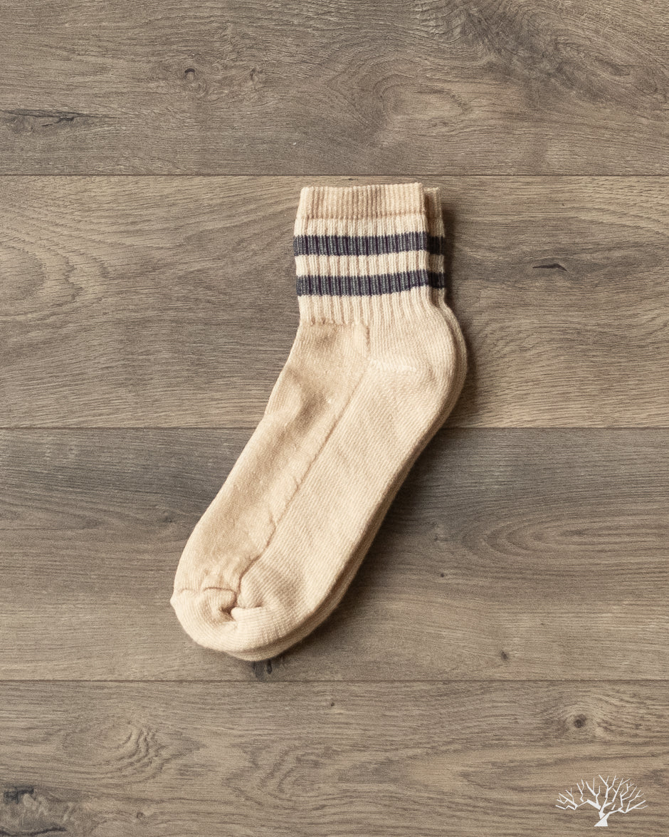 American Trench Merino Activity Quarter Crew sock, beige with two black stripes, on wooden background.