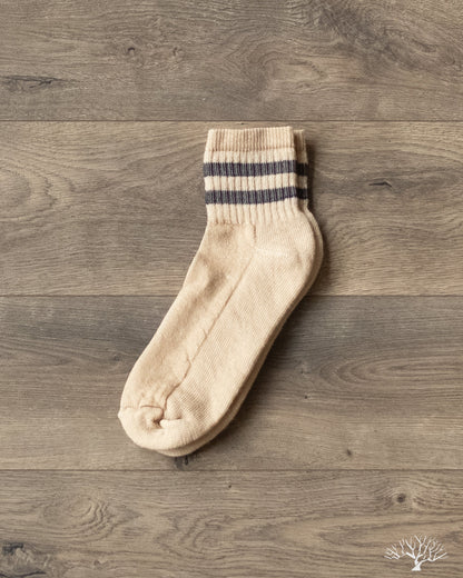 American Trench Merino Activity Quarter Crew sock, beige with two black stripes, on wooden background.