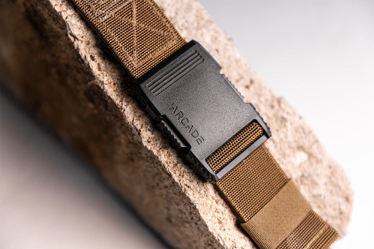 Close-up of the Arcade Hardware Work Belt buckle in black on a brown strap, resting on a textured surface.