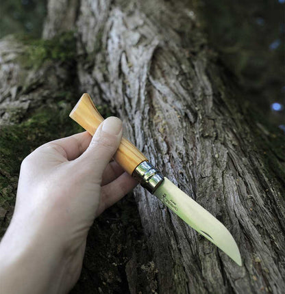 Opinel No.09 Stainless Steel Folding Knife with a light wooden handle, held open in a hand against a tree.