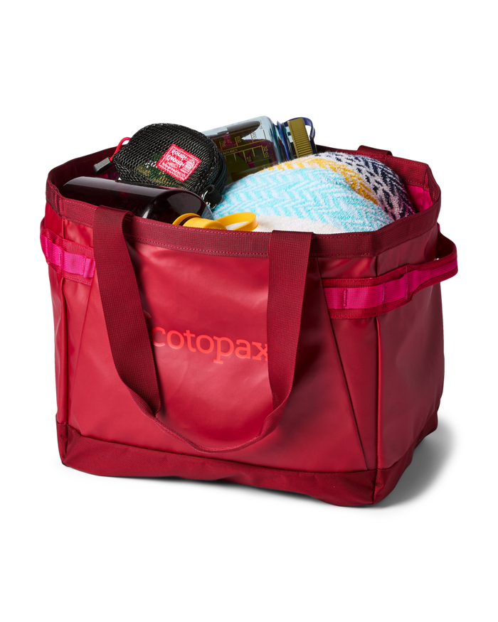 Cotopaxi Allpa 30L Gear Hauler Tote in red, filled with travel essentials like a water bottle and towel.