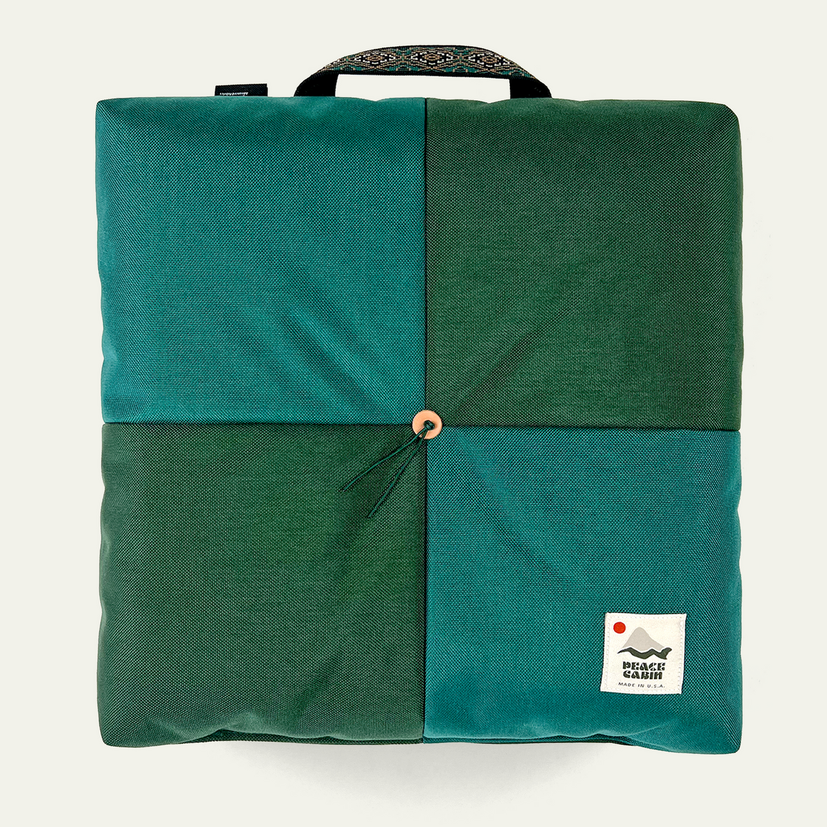 Wanderer 'QUAD' Outdoor Cushion by Media Mercantile, featuring a four-panel design in two shades of green with a central toggle and patterned handle.