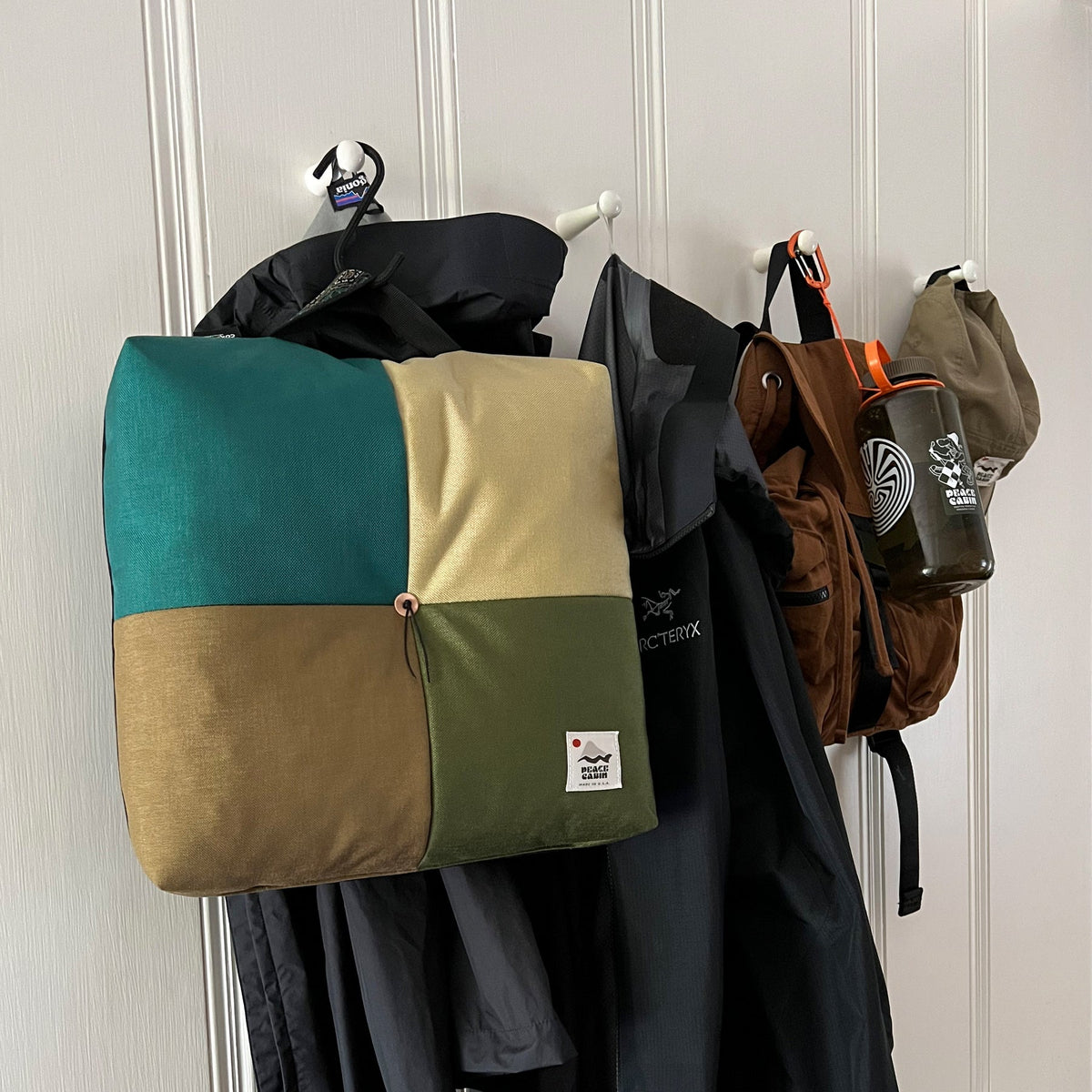 Wanderer 'QUAD' Outdoor Cushion by Media Mercantile, featuring teal, tan, and olive green patchwork, hanging with outdoor gear.