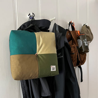 Wanderer 'QUAD' Outdoor Cushion by Media Mercantile, featuring teal, tan, and olive green patchwork, hanging with outdoor gear.