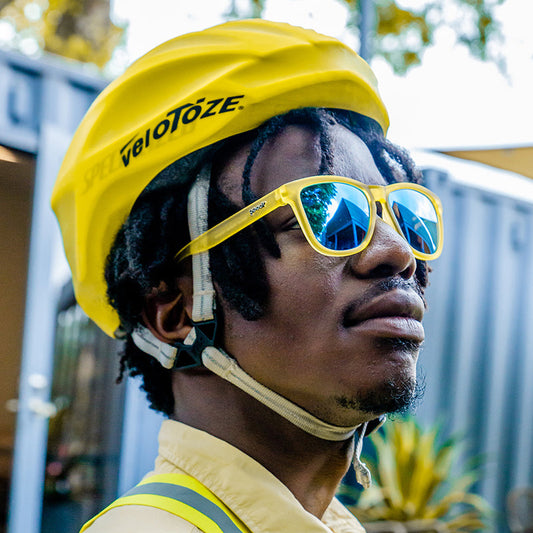 goodr Swedish Meatball Hangover yellow sunglasses with blue lenses, worn by a cyclist in a yellow helmet.