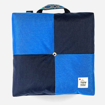 Wanderer 'QUAD' Outdoor Cushion from Media Mercantile, blue checkerboard pattern with a handle and 'Peace Cabin' tag.