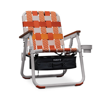 PARKIT Voyager Sunkissed beach chair with orange, white, and peach checkered webbing, wooden armrests, cup holder, and storage bag.