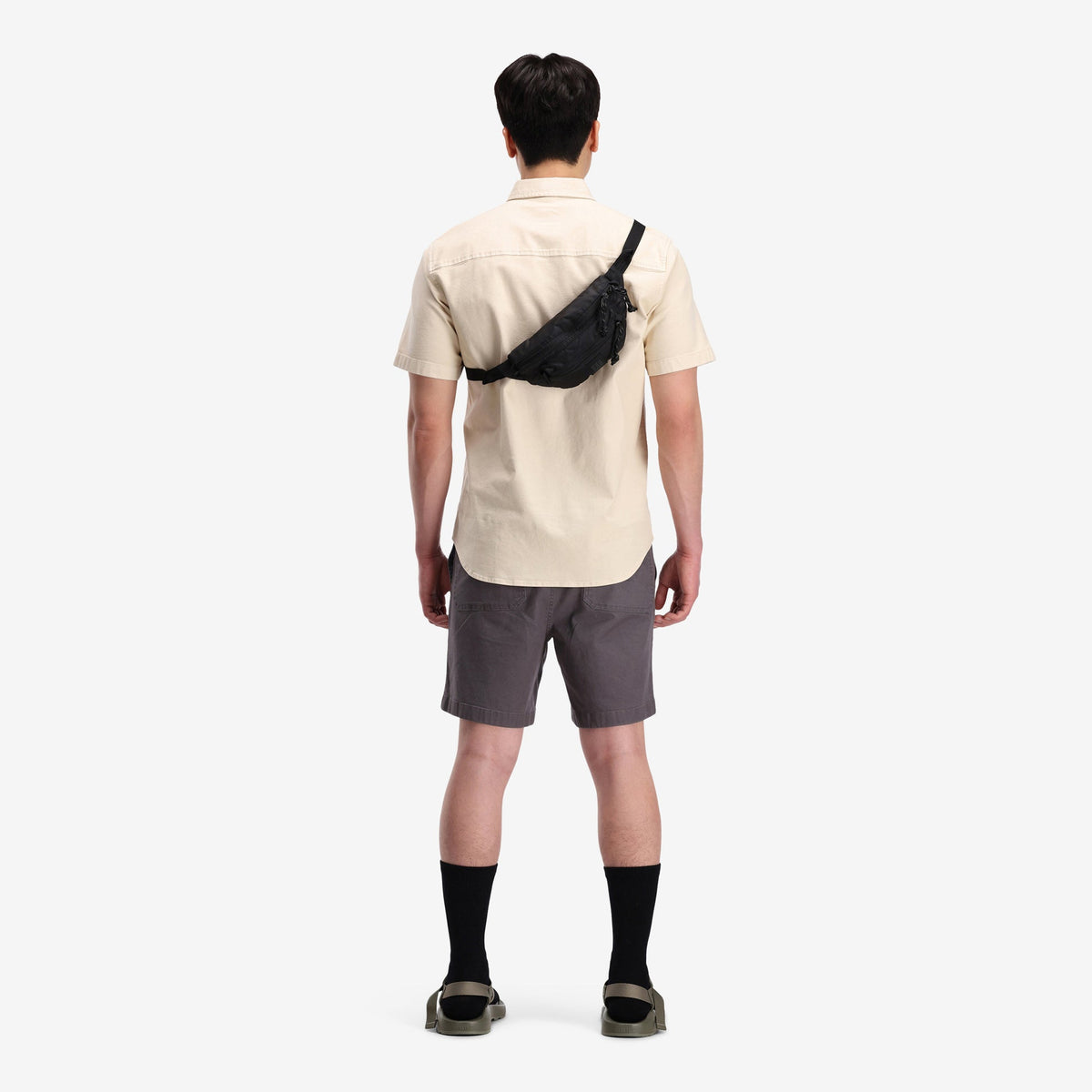 Topo Designs Mountain Waist Pack in black, worn diagonally across a man's back over a beige shirt.