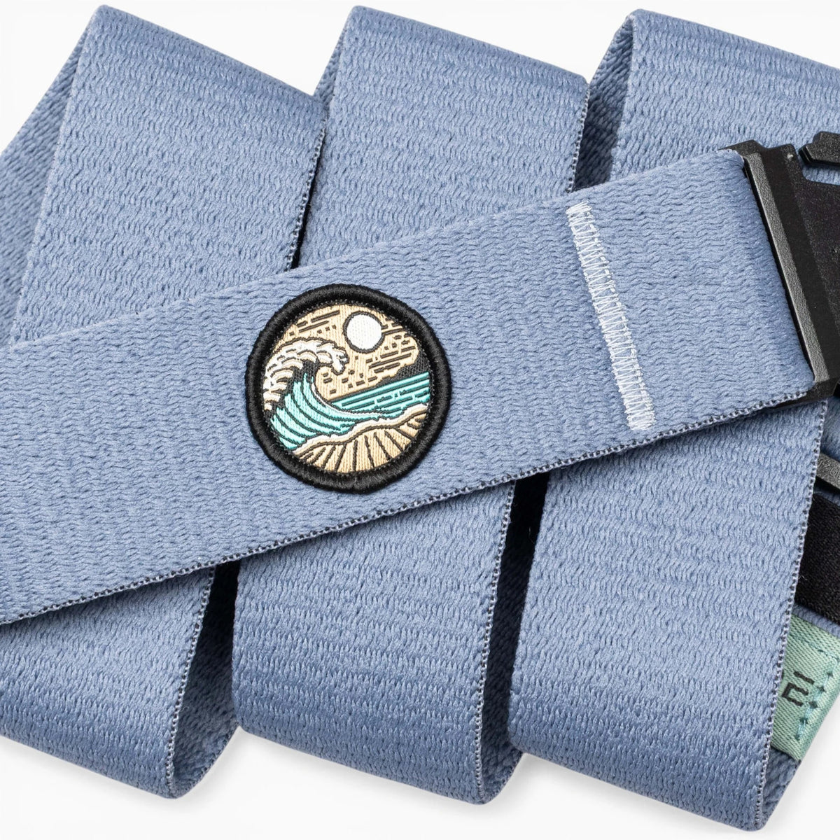 Arcade Belts Save the Waves Stretch Belt in light blue, featuring a circular embroidered patch with an ocean wave and sun design.