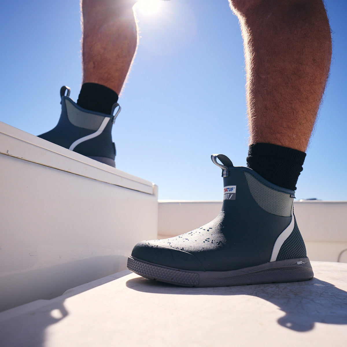 Close-up of XTRATUF Men's Ankle Deck Boot Sport in Stormy Blue with water drops, on a sunny boat deck.