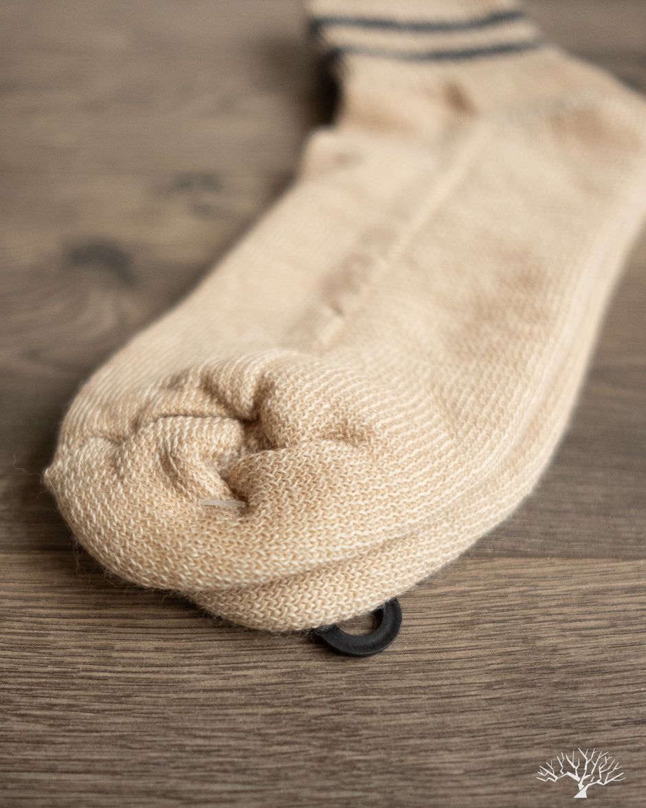 American Trench Merino Activity Quarter Crew sock in light tan, showing knit texture and black tag on wooden surface.