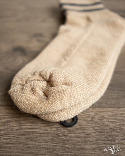 American Trench Merino Activity Quarter Crew sock in light tan, showing knit texture and black tag on wooden surface.