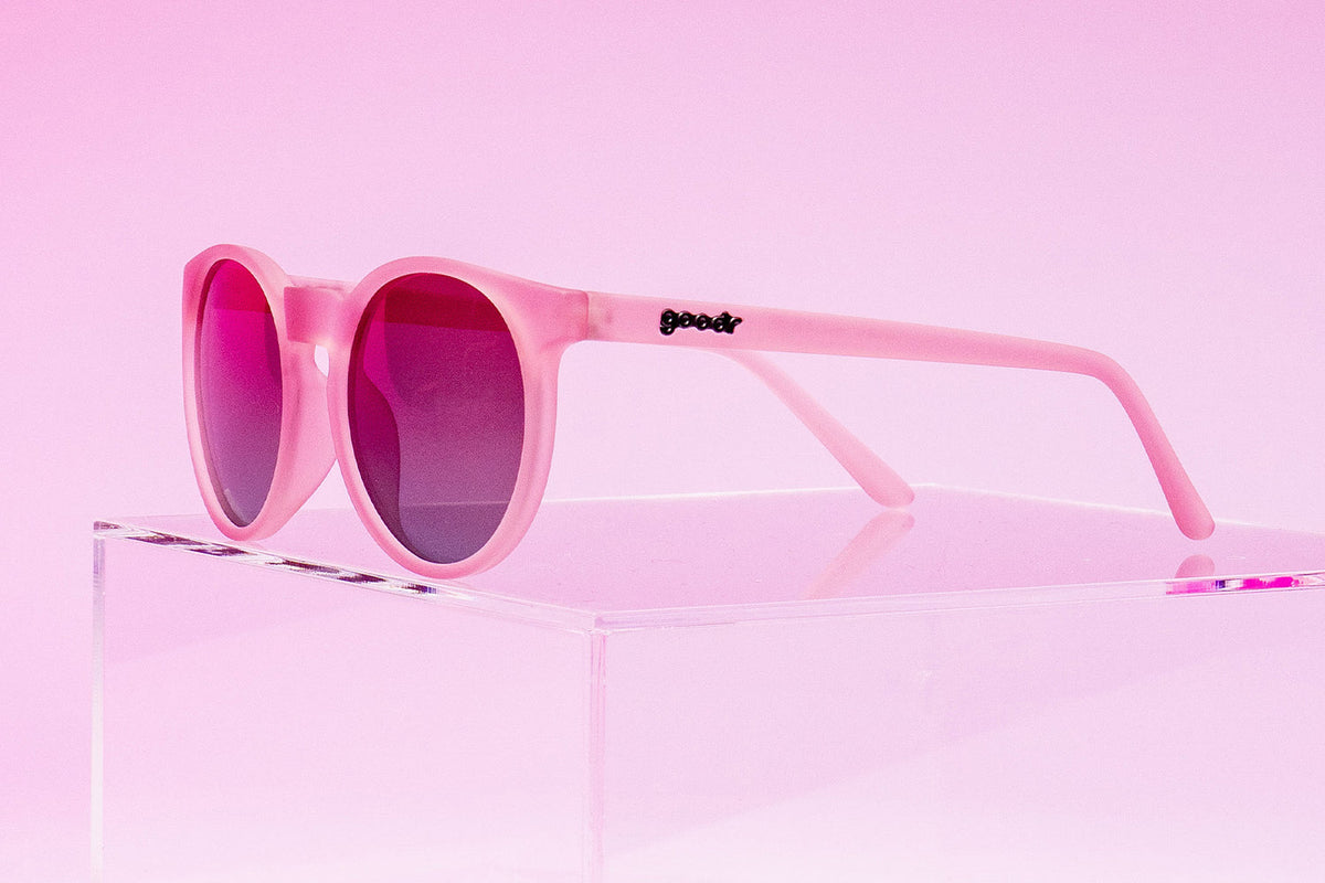 Mauve Mood Board goodr sunglasses with pink frames and dark lenses on a clear stand against a pink background.