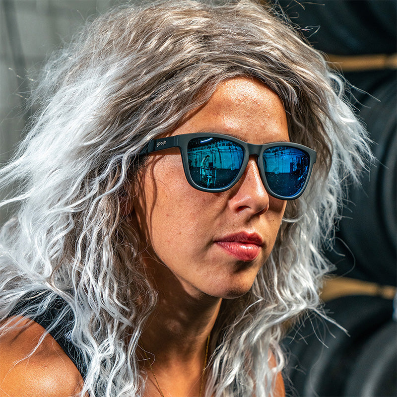 Woman with curly grey hair wearing Mick and Keith's Midnight Ramble goodr sunglasses with black frames and blue mirrored lenses.