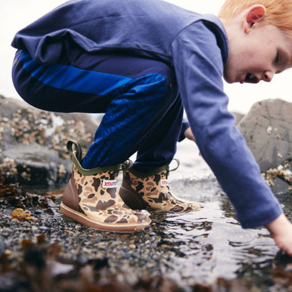Child in XTRATUF Kids' Ankle Deck Boots - Stone, crouching and exploring a rocky tide pool.