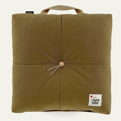 Wanderer 'QUAD' Outdoor Cushion by Media Mercantile, olive green with a handle, central wooden button, and brand tags.