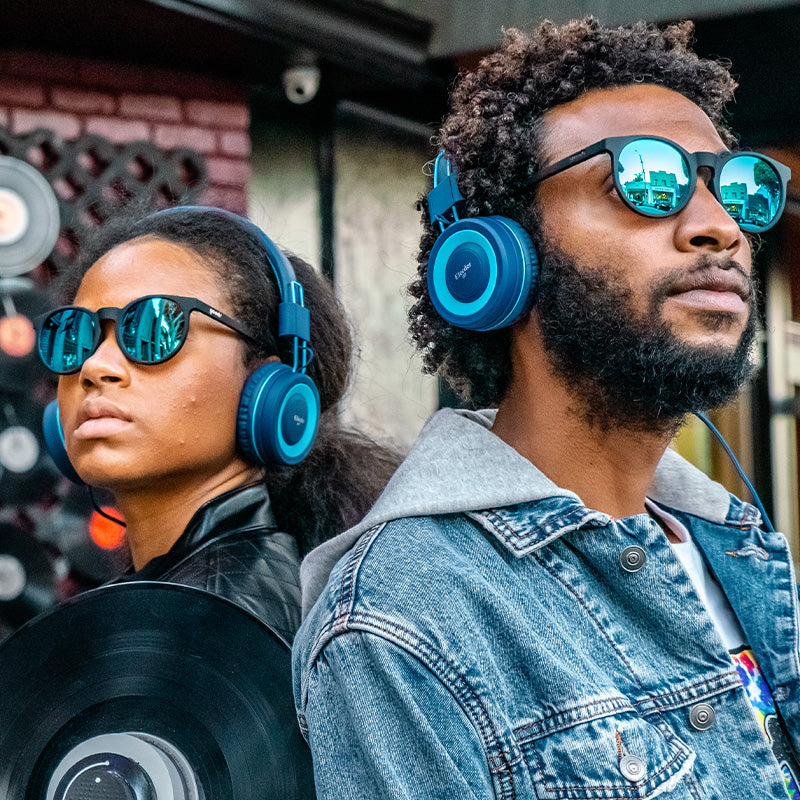 Two people wearing Midnight Ramble at the Circle Bar goodr sunglasses and blue on-ear headphones, urban scene.