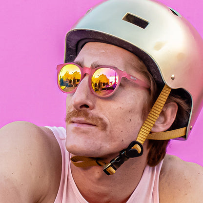 Man in gold helmet, pink tank top, and 'Influencers Pay Double' pink goodr sunglasses with mirrored lenses reflecting scenery.