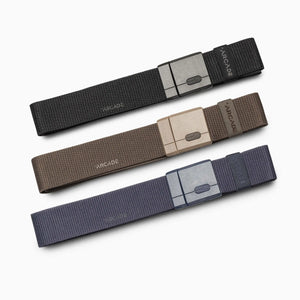Arcade Atlas Stretch Belts in black, tan, and dark blue, featuring flat, low-profile buckles.