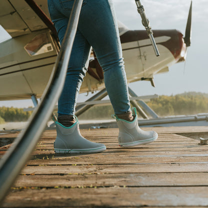 Women's Ankle Deck Boot - Fig | XTRATUF light gray boots on a person standing on a wooden dock with a floatplane.
