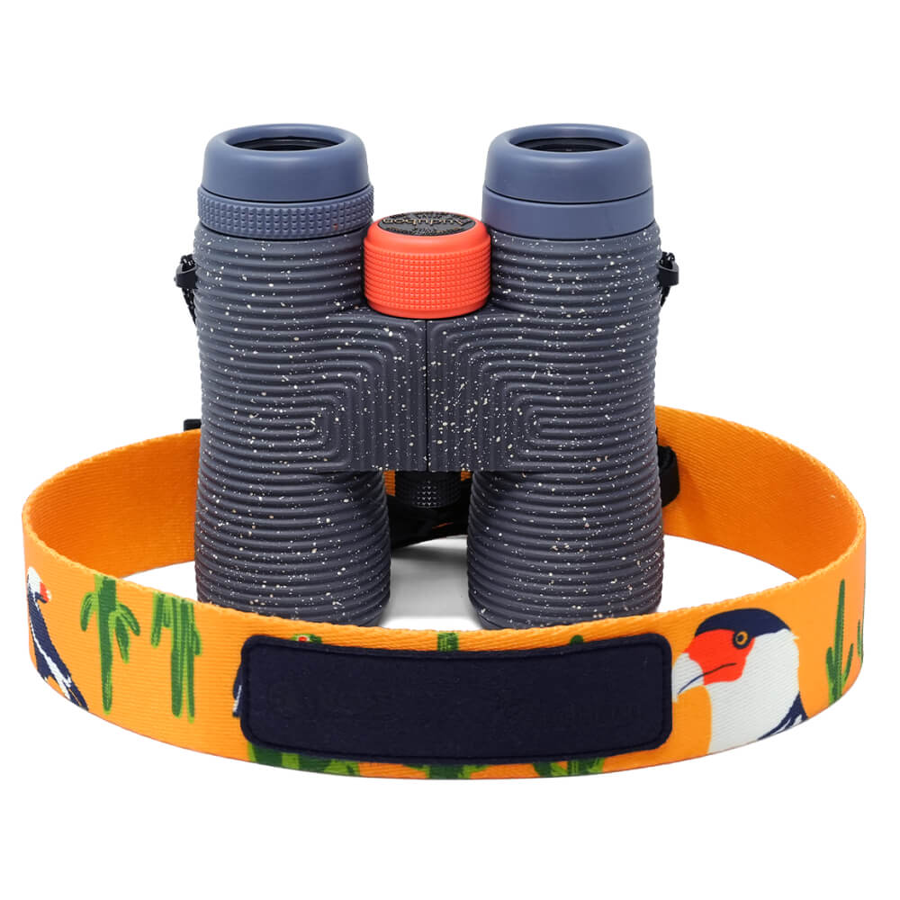Nocs Provisions Field Issue 8x42 Binoculars in dark gray with an orange focus wheel and a colorful bird and cactus strap.