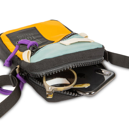 Topo Designs Mini Shoulder Bag, multi-color (yellow, black, light blue) with purple cord, open zipper revealing phone and sunglasses.