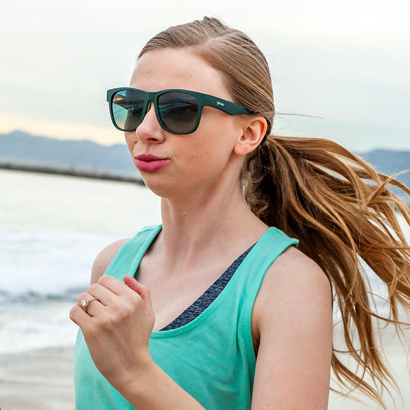 Woman running on beach wearing goodr Mint Julep Electroshocks sunglasses.