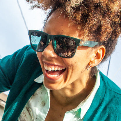A person laughs joyfully, covered in dirt, wearing Mint Julep Electroshocks goodr sunglasses with turquoise lenses.