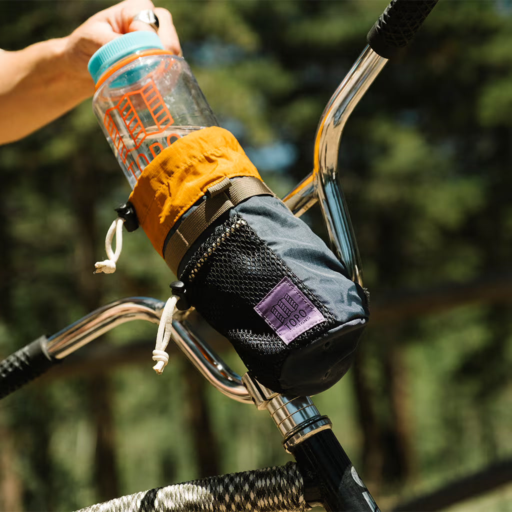 Topo Designs Mountain Hydro Sling in gray and orange attached to a bike handlebar, holding a clear water bottle.