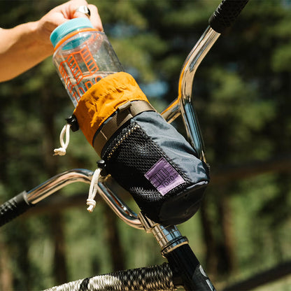 Topo Designs Mountain Hydro Sling in gray and orange attached to a bike handlebar, holding a clear water bottle.