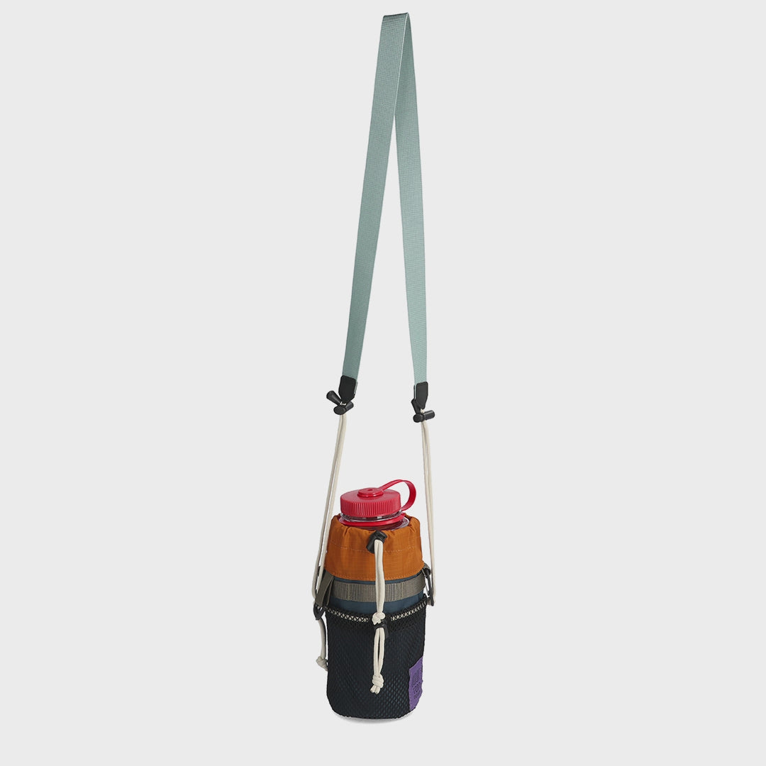 Topo Designs Mountain Hydro Sling with a red water bottle, featuring a multi-color design and light blue adjustable strap.