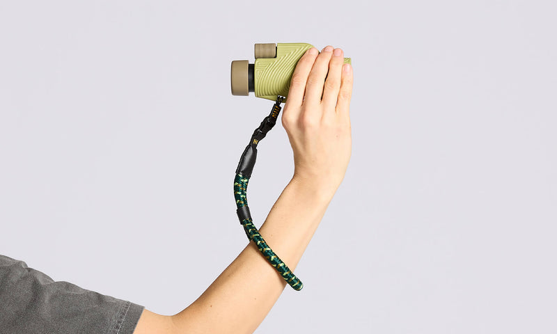Nocs Provisions NocLoc Approach Wrist Loop, a green & black braided strap, worn on a wrist holding a green monocular.