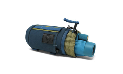 Blue and olive green Tube Caddy | Nocs Provisions, carrying a blue monocular, isolated on a white background.