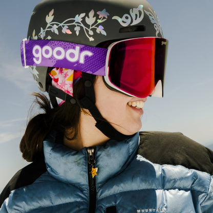 Smiling person in goodr ski helmet, purple goodr goggles, blue puffer jacket. For Vintage Snow Suit Ambitions.